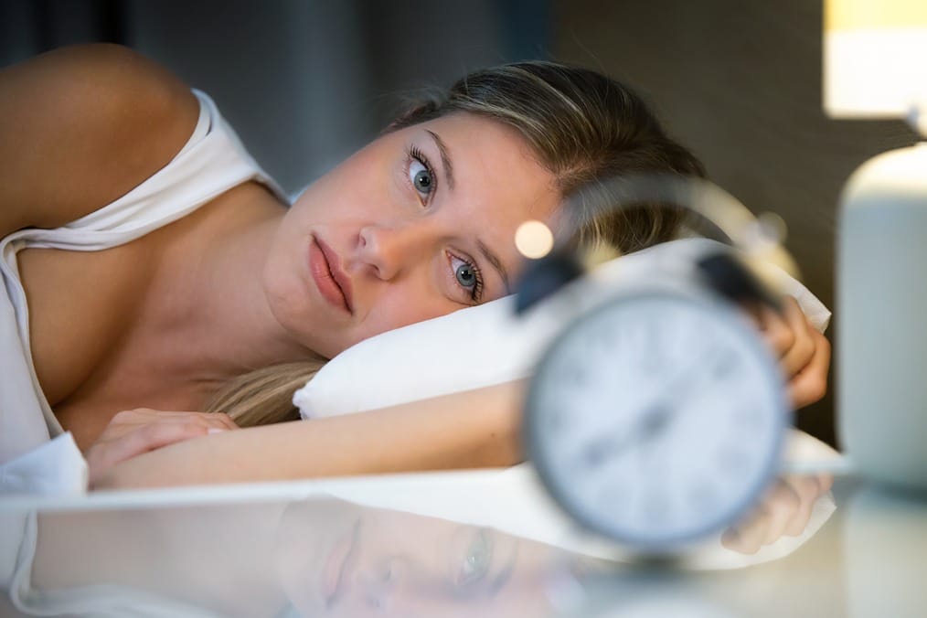 Eine Frau im Bett schaut auf ihren Wecker, um die Wirkung von CBD bei Schlafstörungen zu symbolisieren.