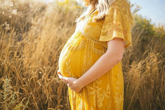 Femme enceinte en robe jaune tenant son ventre dans un champ, évoquant le CBD et la grossesse